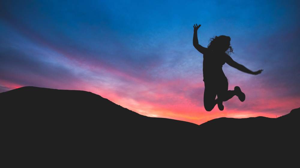 Silhouette of a woman jumping with a mountain behind her at sunset, symbolizing the liberating power of English language learning through engaging song-based activities.